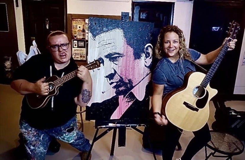 Megan Deprey, left, often paints as Dani Maus, right, performs. Here they are shown with instruments beside a portrait by Deprey.