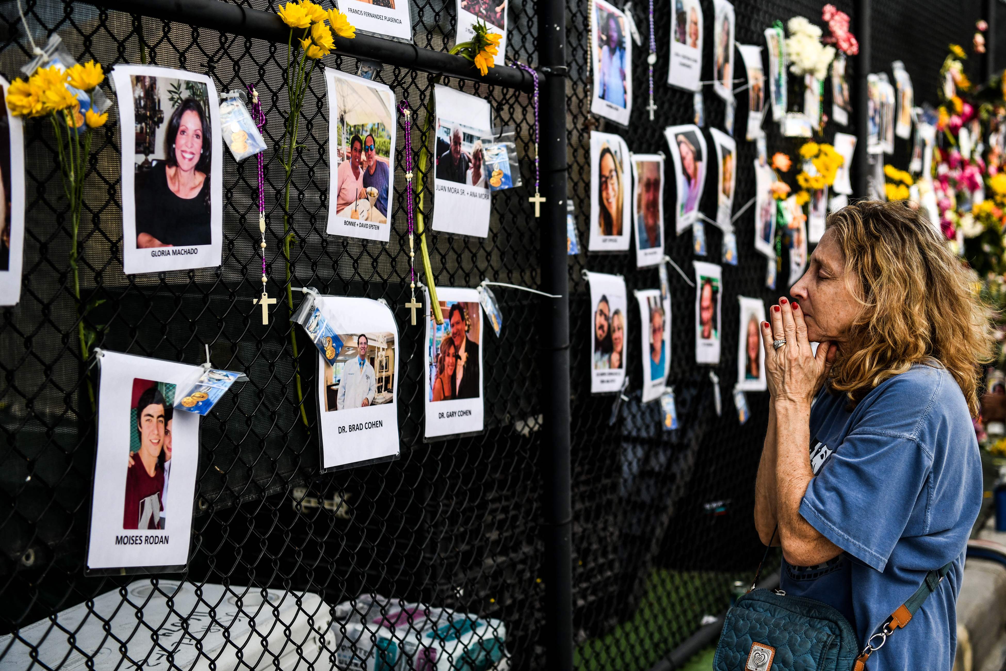 A woman prays in front of photos at the makeshift memorial for the victims of the building collapse, near the site of the accident in Surfside, Fla., north of Miami Beach on June 27, 2021.