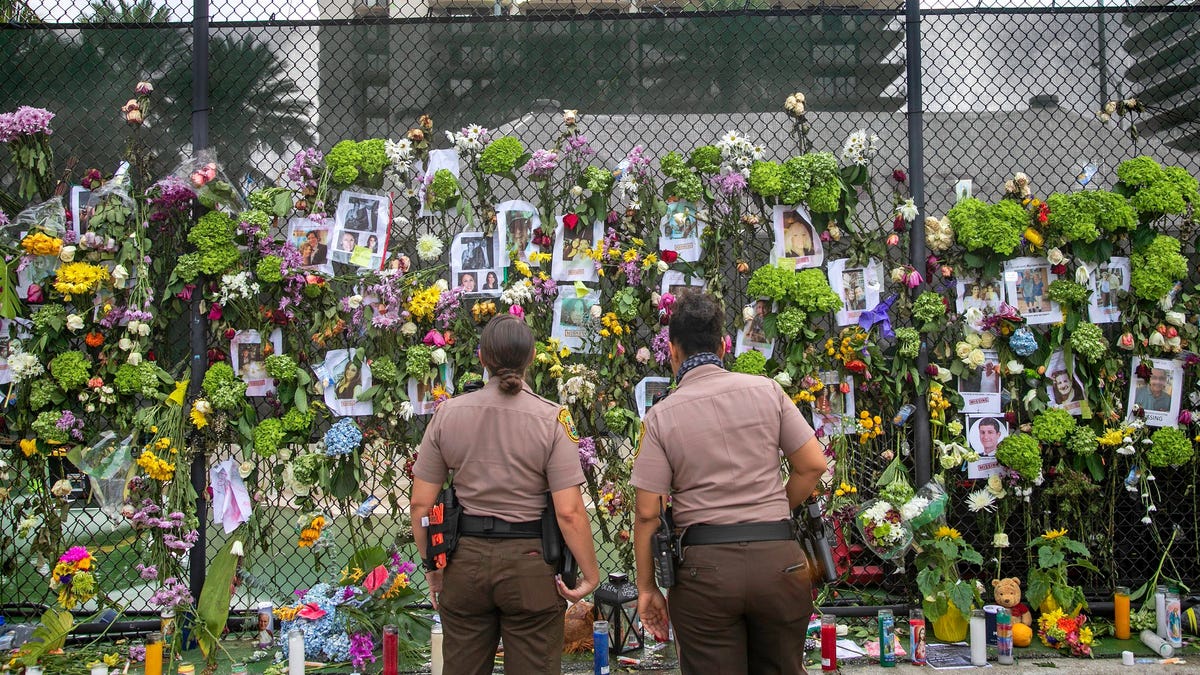 Miami-Dade police officers look at photos of missing residents on a fence in front of Champlain Towers South condo in Surfside, Fla. Tuesday, June 29, 2021.