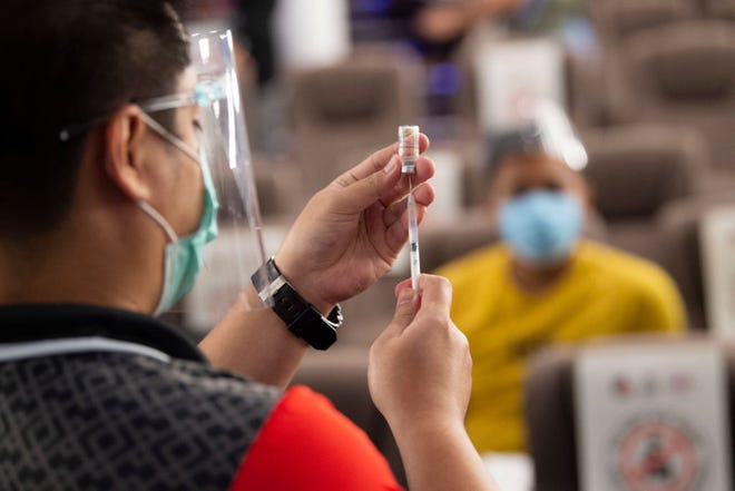 A health worker (left) prepares a vial of Chinese Sinovac vaccine against Covid-19 coronavirus inside a movie theatre turned into a vaccination centre in Taguig City suburban Manila on June 14, 2021. (Ted Aljibe/AFP via Getty Images/TNS)