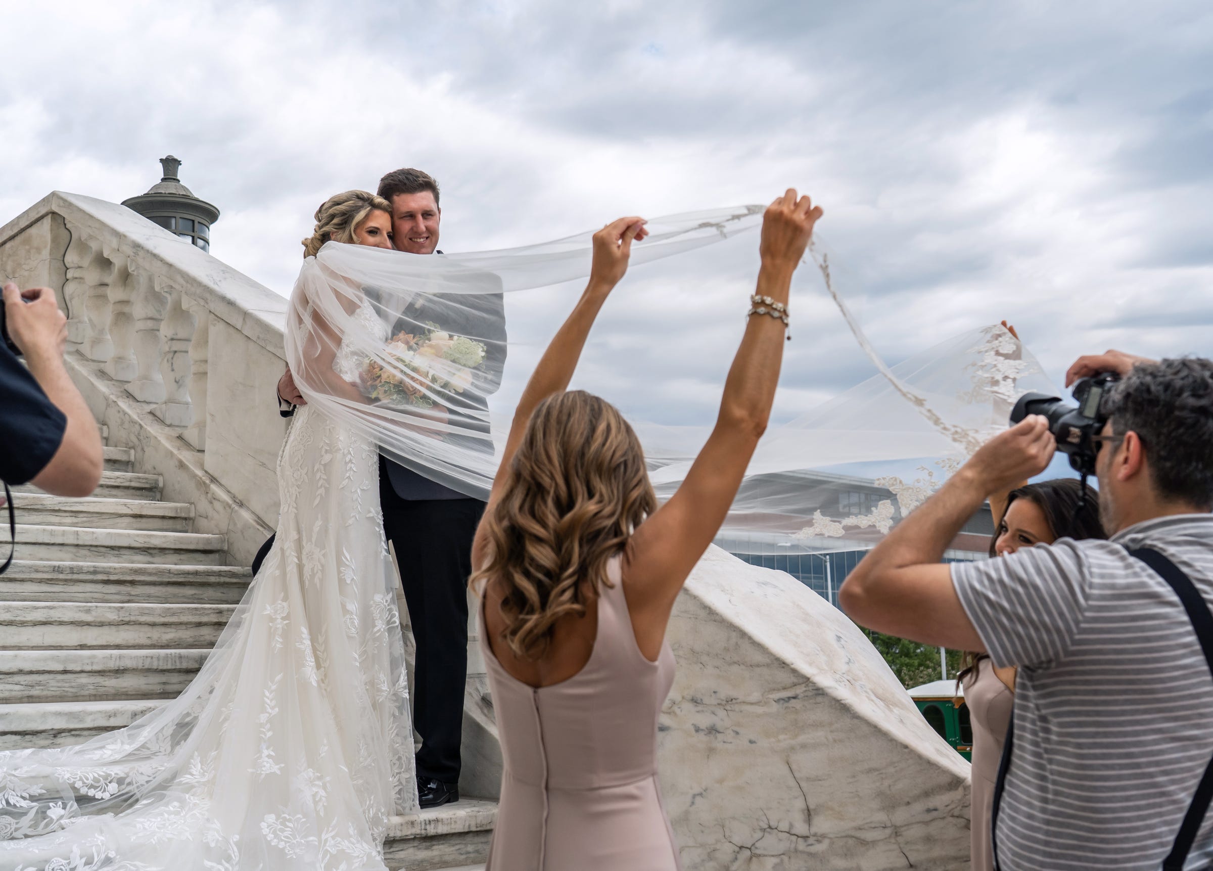 Rebecca McNally and husband, Sean McNally, of Trenton, pose for a photo as Rebecca's sister and bridesmaid Jackie Naik holds the veil for photographer Arthur Safarov on their wedding day on the staircase at the rear of the Detroit Institute of Arts on Saturday, June 19, 2021.