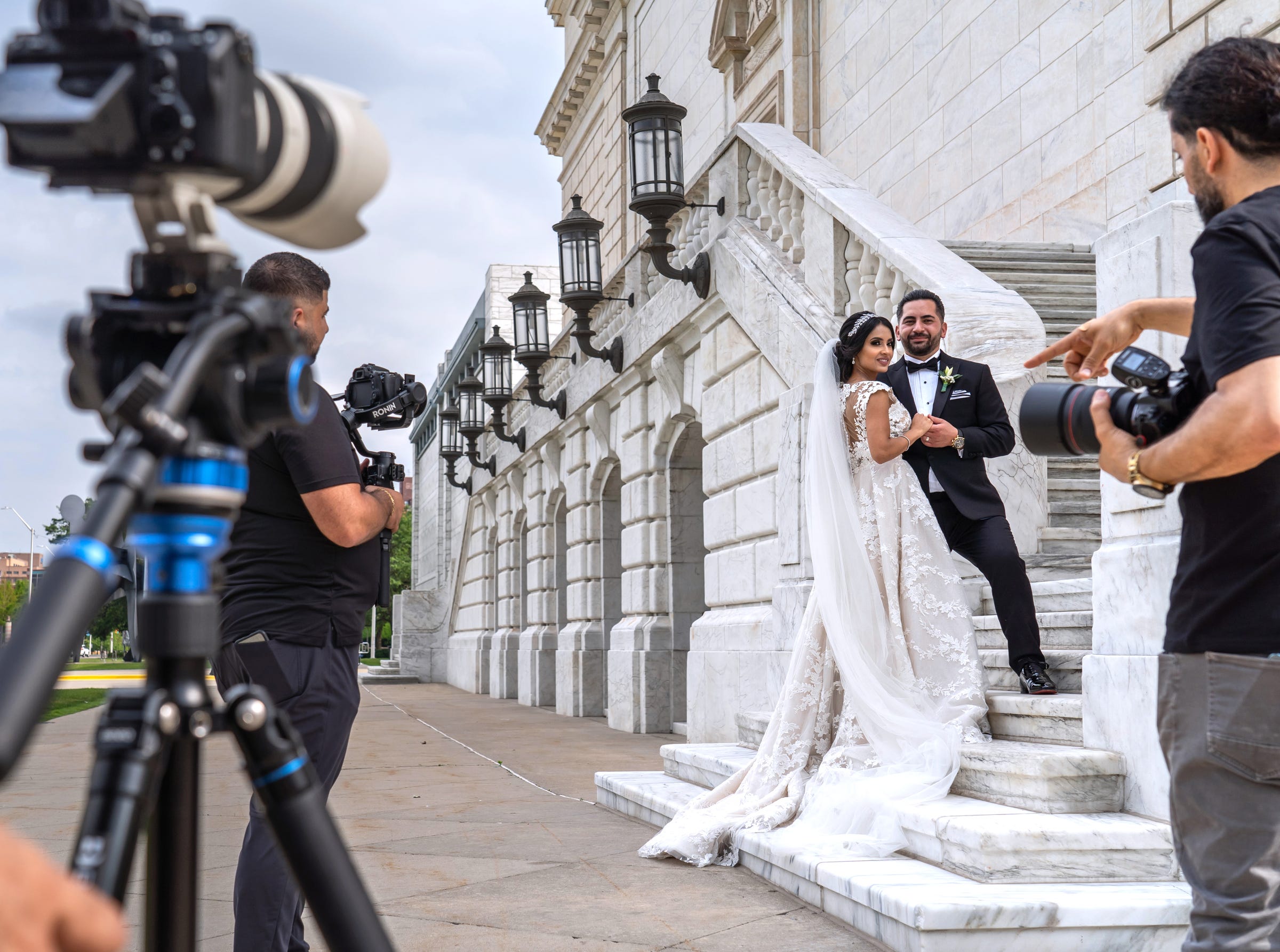 Photographer Bill Mcdad directs bride and groom Ibtisam Shukr of Dearborn and Ali Shukr as a video team works alongside during a photo shoot on their wedding day on the staircase at the rear of the Detroit Institute of Arts on Friday, June 18, 2021 before they headed to their reception at the Eastern Market.