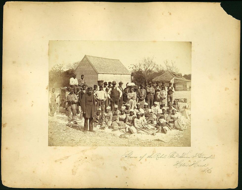 A photograph showing a group portrait of African-American men and women on a plantation on Hilton Head Island during the Civil War. Photograph by Henry P. Moore.