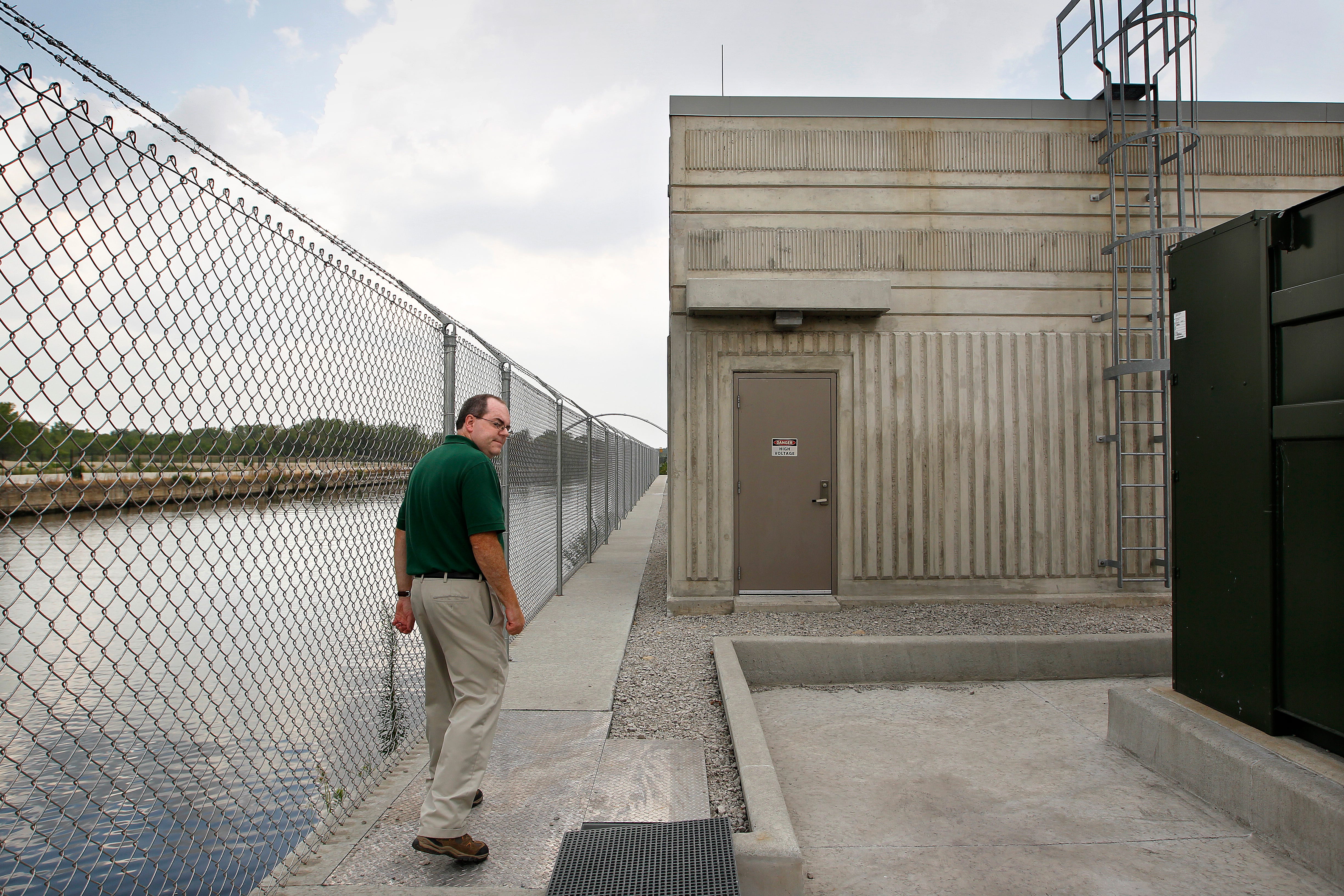 CARP_BARRIER. NWS, PORTER, 4. - Charles Shea. project manager, walks along the fenced off area of the Army Corps of Engineers' Electric Dispersal Barriers' monitoring station on the Chicago Sanitary and Ship Canal in Lockport, Illinois near Chicago. The barriers are designed to prevent inter-basin transfer of fish between the Mississippi River and the Great Lakes basins via the canal. July 19, 2012. GARY PORTER/GPORTER@JOURNALSENTINEL.COM