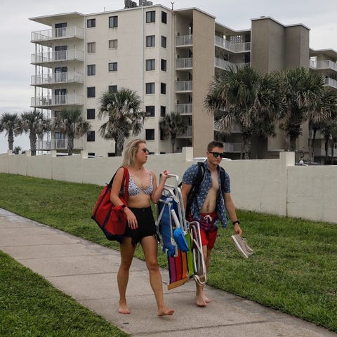 A pair of beachgoers walk in front of an oceanfron