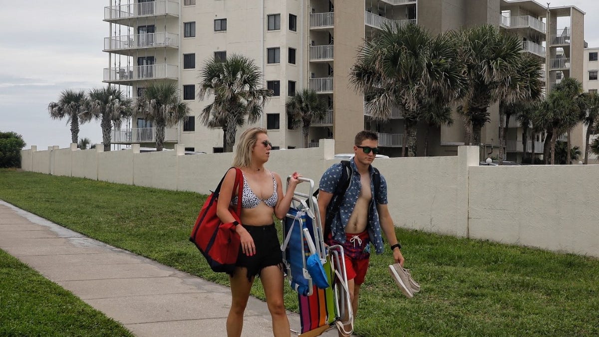 A pair of beachgoers walk in front of an oceanfront high-rise condo complex where temporary bracing has been installed for each of the balconies in New Smyrna Beach on Wednesday, July 7, 2021. The two-building seven-story complex is set to undergo an extensive repair and renovation project beginning in early August, said Tom Ryon, a consultant to the property's condo owners association.