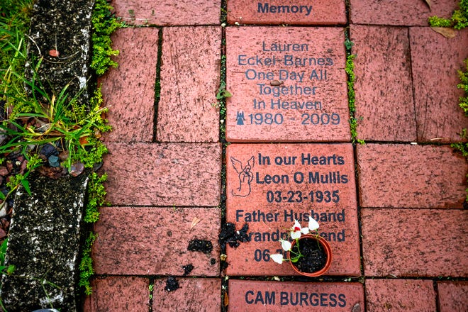 A pot of white flowers rests on a memorial stone in a maze in the Survivors of Suicide Memory Garden in Cofrin Nature Park in Gainesville.