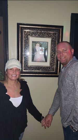 Belinda and her Husband standing in Front of a picture of her grandmother, Ellen