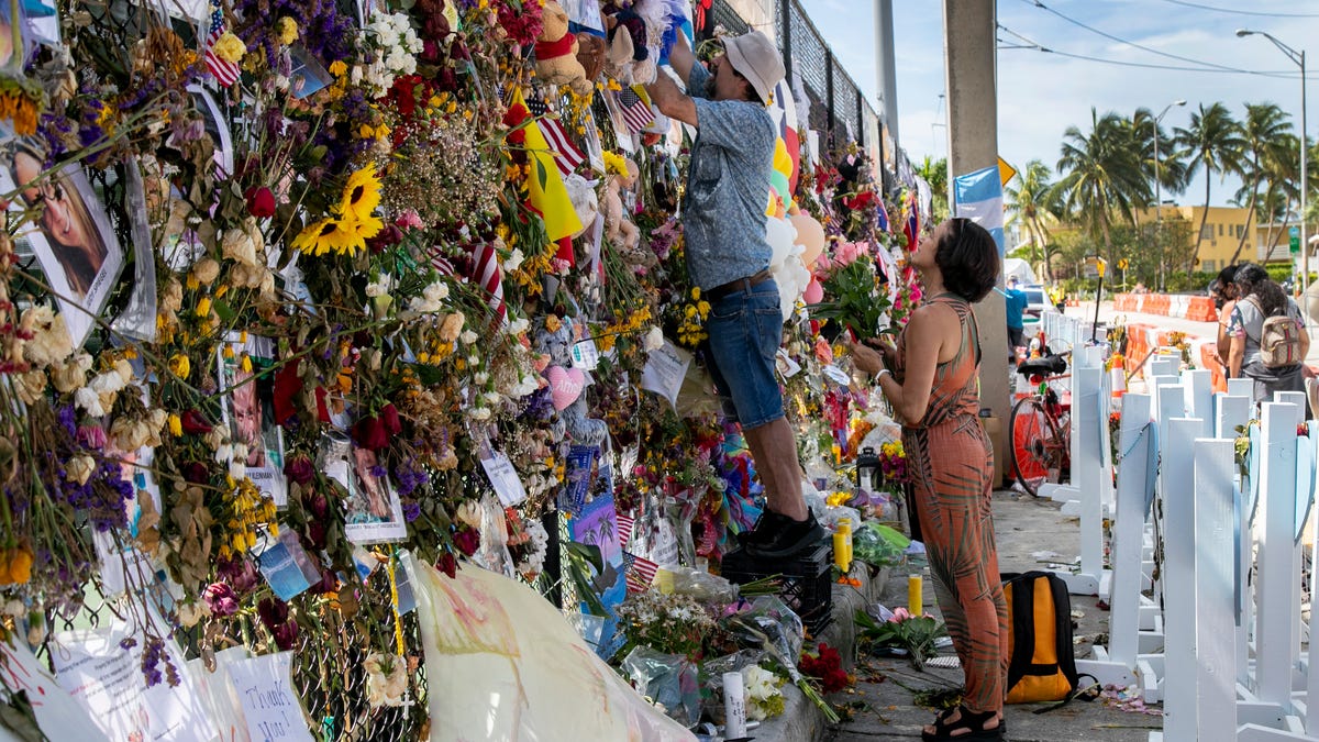 A couple adds fresh flowers to the memorial wall at the site of the Champlain Towers South collapse on Wednesday, July 14, 2021, in Surfside. 