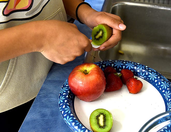 Oakland Middle School eighth grader Cassidy Childs, 13, removes a kiwi peel on Friday during a class called Kids in the Kitchen, a partnership with 4-H.