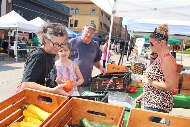 Monica Peitz picks out a tomato at the Wilson Farm Produce booth while Zoe Mattern and Alan Peitz look on during the Perry Farmers Market on Thursday, July 15, 2021.