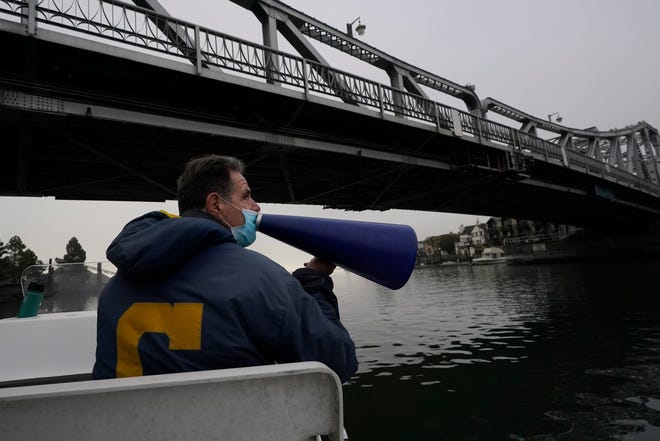 Coach Mike Teti speaks into a megaphone toward rowers practicing in the Oakland Estuary in Oakland, Calif., on Nov. 19, 2020.