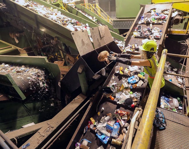 FILE — A worker removes plastic bags from a conveyor belt of recyclable goods at the Waste Management JMK Fibers recycling facility in Tacoma in July 2021. A Waste Management driver shortage led to thousands of missed pickups of recycling and yard waste for customers in unincorporated Kitsap County in the summer and fall of 2021, the state Utilities and Transportation Commission found.