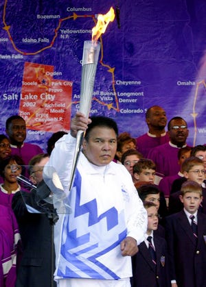 Boxing legend Muhammad Ali holds up the first Olympic torch lit from the cauldron in front of a map showing the torch's route during a ceremony at Centennial Olympic Park in Atlanta Tuesday, Dec. 4, 2001.
