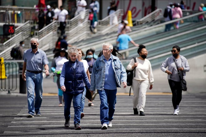 Masked and unmasked pedestrians walk across Las Vegas Boulevard, in Las Vegas. Elected officials in tourism-dependent Las Vegas worried Tuesday about public health and the economic effects of a spike in COVID-19 cases, particularly the highly contagious delta variant.