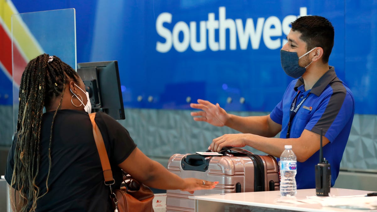 In this June 24, 2020, file photo, Southwest Airlines employee Oscar Gonzalez, right, assists a passenger at the ticket counter at Love Field in Dallas.