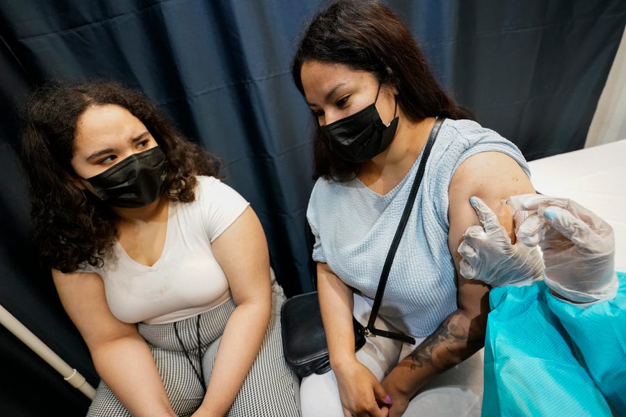 A health care worker inoculates Evelyn Pereira, right, of Brooklyn, New York, with the first dose of the Pfizer COVID-19 vaccine as her daughter Soile Reyes, 12, looks on.