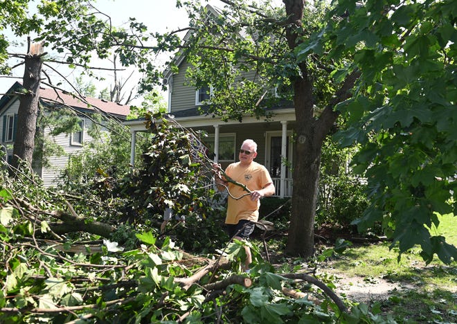 Keith Christoff, 55, of Armada helps his neighbor clean up debris and fallen trees in front of his house on North Fulton Street.