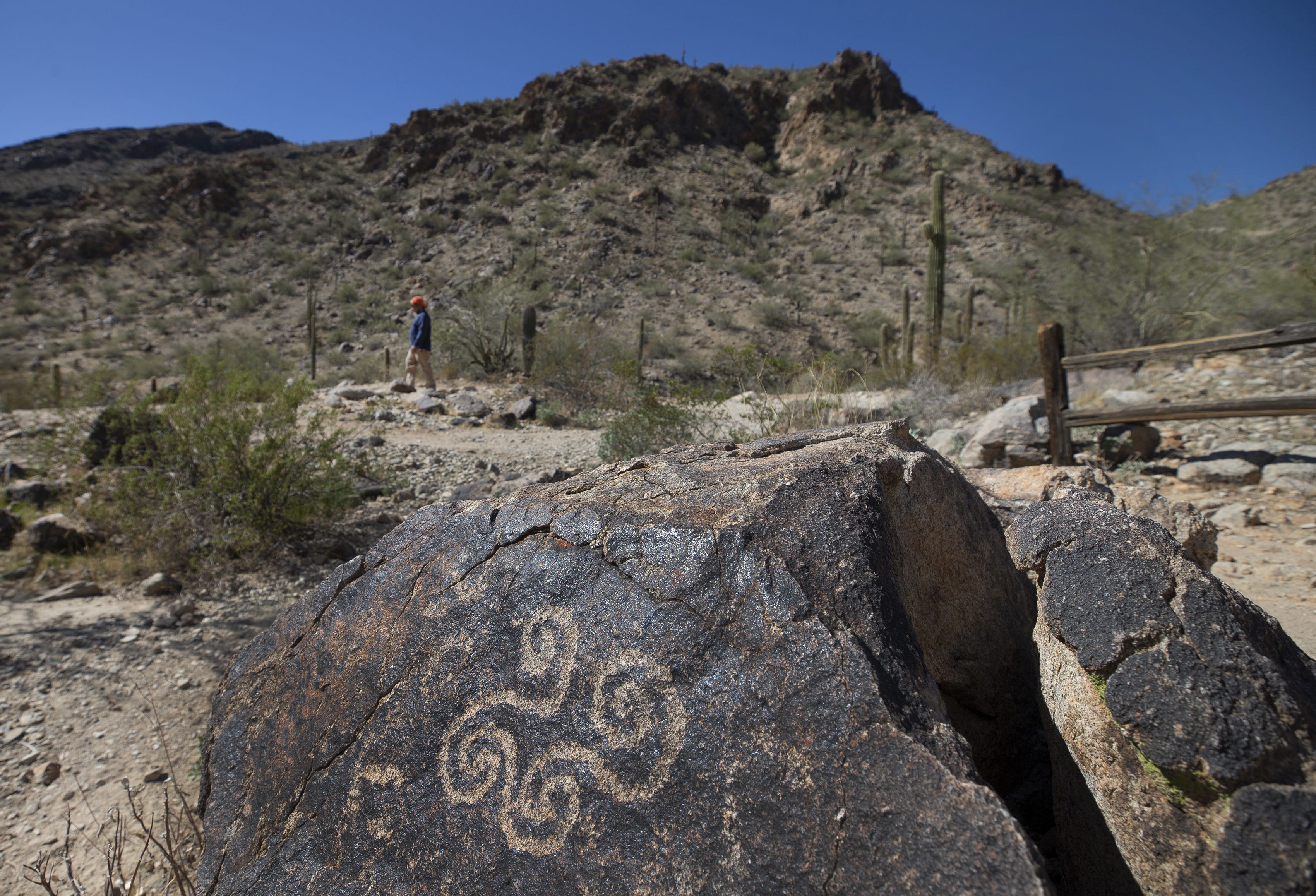 Hikers on Telegraph Pass Trailhead walk pass petroglyphs created by the Huhugam at South Mountain Park in Phoenix.
