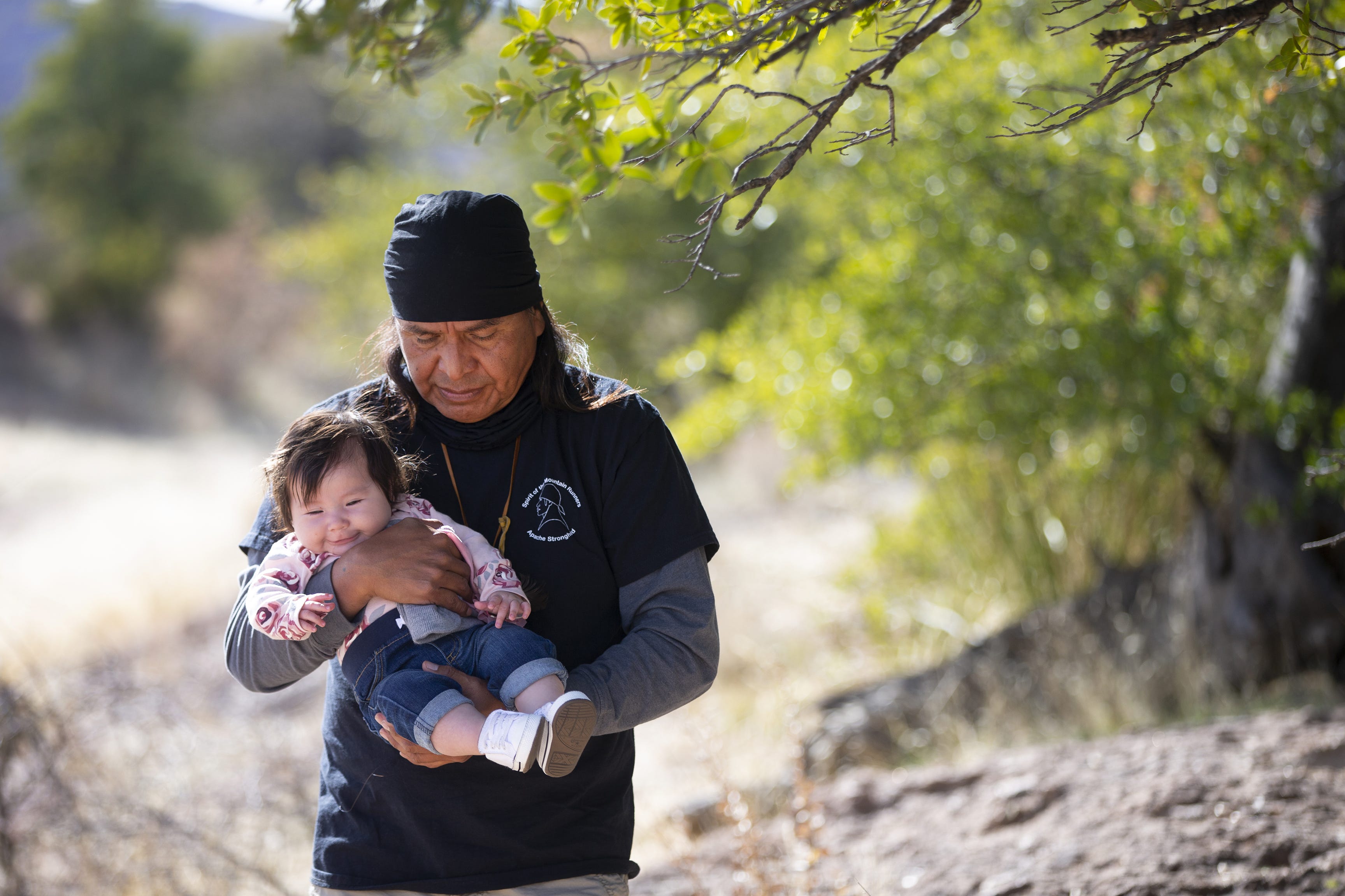 Former San Carlos Apache Tribe Chairman Wendsler Nosie Sr. and leader of Apache Stronghold walks with his 4-month-old granddaughter, Sha'yu Nosie-Frejo, at Oak Flat campground.