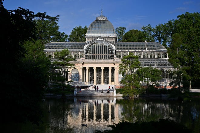 People sit on the stairs in front of the Palacio de Cristal at the Retiro Park in Madrid on May 25, 2020, as the park's gates reopen amid the COVID-19 pandemic.