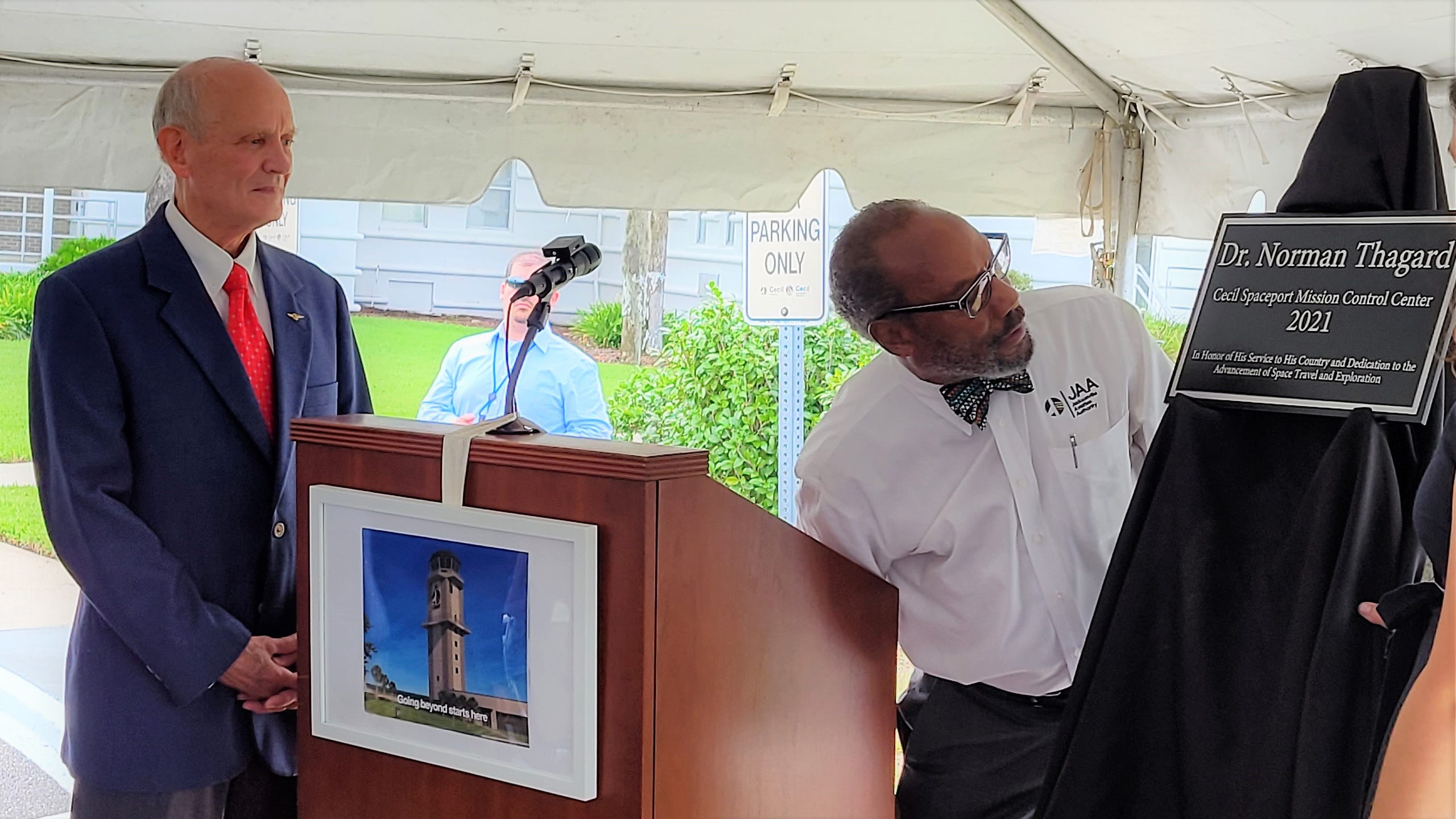 Jacksonville Airport Authority external affairs director Michael Stewart (right) unveils the plaque naming Cecil Spaceport's new tower and mission control after Jacksonville native and NASA astronaut Norman Thagard.