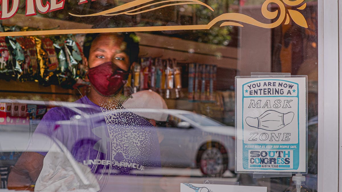 A store employee wearing a mask cleans a window with a sign requesting customers put on masks at a shop on South Congress Avenue. Travis County in Texas moved back to Stage 4 of COVID rules and health officials are asking residents who have yet to receive a coronavirus vaccine to sign up for one immediately.