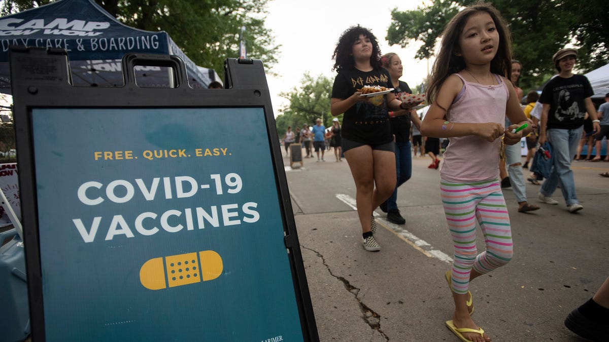 People walk past a sign for COVID-19 vaccine information at a Larimer County Heath and Environment booth at Taste of Fort Collins in Fort Collins, Colo. on Saturday, July 24, 2021.