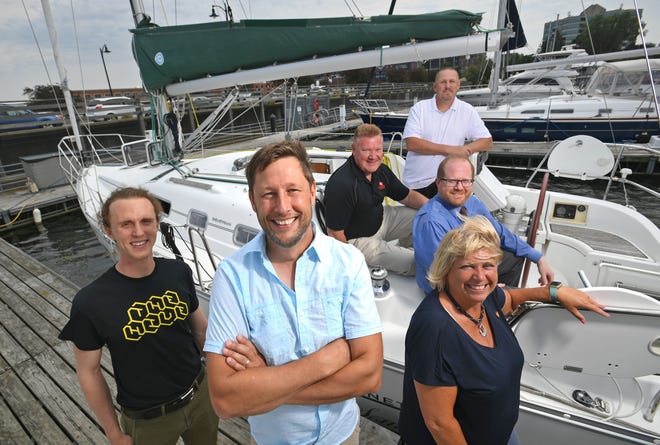 Boater and businessman Scott Hitz, foreground, center, has benefitted from the Northwest Pennsylvania Innovation Beehive Network, a group of business and entrepreneurship experts from four local universities and the Erie County Library system that provides help for startups in the Erie region. Hitz is the owner of Your Sailing Adventure, taking clients on sailing trips on his 32-foot-long Beneteau sailboat, background. Shown Tuesday at Wolverine Marina on Erie’s bayfront are, from left: Patrick Moran, emerging technologies librarian at Blasco Memorial Library; Hitz; Tony Peyronel, executive director for entrepreneur development at Edinboro University of Pennsylvania; Brian Fuller, director of the Innovation Entente Lab at Mercyhurst University; Jacob Marsh, industry relations coordinator at Penn State Behrend; and Kathy Roach, entrepreneurship coordinator at Gannon University.