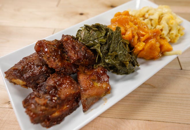 A plate of BBQ rib tips, collard greens with smoked turkey, candied yams, and East coast style macaroni & cheese at Queen City Soul Kitchen.
