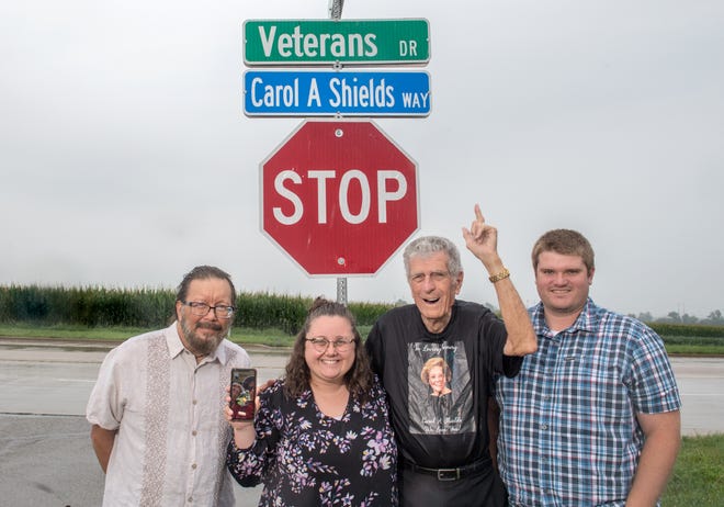 Family members of Carol A. Shields gather at the sign naming a section of Veterans Drive at Griffin Avenue in her honor. Shown left to right are: oldest son, Doug Shields; granddaughter Katelyn McDougall; husband, Harland Shields; and grandson Austin McDougall. On the cellphone are daughter-in-law Lori Shields and youngest son, Dave Shields.