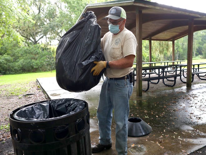 Mike Hutchins, a parks and events worker for the City of Gainesville Parks, Recreation and Cultural Affairs Department, wears a mask as he replaces a trash bag in Cora Roberson Park on Monday.