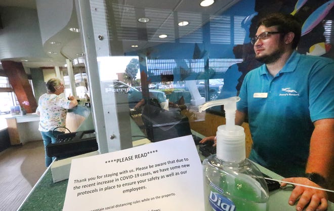 Front desk clerk Shane Treudt works behind a clear plastic screen at Perry's Ocean Edge Resort in Daytona Beach Shores on Tuesday, Aug. 3, 2021. After relaxing some of its COVID-related procedures earlier this summer, the hotel has re-instituted stricter guidelines in the wake of a recent significant increase in COVID-19 cases and hospitalizations.