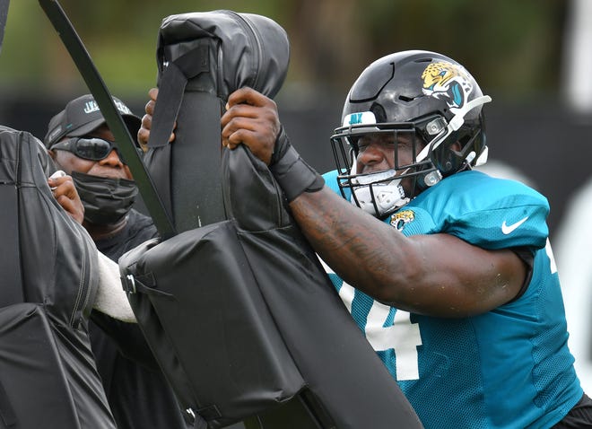 Jaguars OL (74) Cam Robinson hits the sled as offensive line coach George Warhop looks on during drills at training camp on the practice fields outside TIAA Bank Field in Jacksonville, FL Tuesday, August 3, 2021. Tuesday was the first day of players wearing pads for practice.