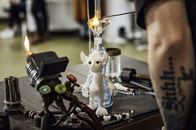Chris Vela, a contemporary marijuana glass artist, works on a piece in studio, affixing a glass goblin character to a pipe – a collaboration with artist Mike Shelbo.