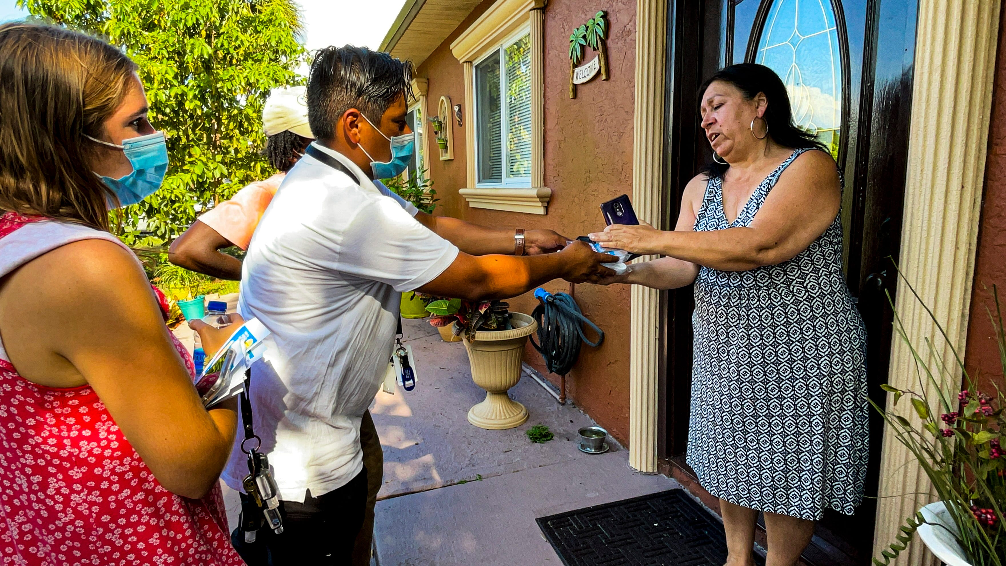 Healthcare Network worker Osman Lopez Hernandez hands a woman a packet of masks.