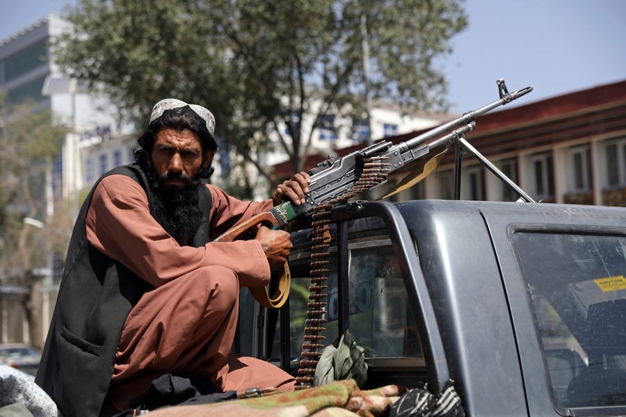 A Taliban fighter sits on the back of vehicle with a machine gun in front of the main gate leading to the Afghan presidential palace, in Kabul, Afghanistan, Monday, Aug. 16, 2021. The U.S. military has taken over Afghanistan's airspace as it struggles to manage a chaotic evacuation after the Taliban rolled into the capital.