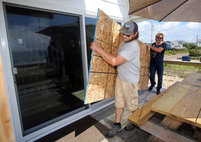 James Masog, center, and Gary Tavares, right, move particle board into place to board up the sliding glass doors of a clients house in Charlestown, R.I., ahead of Hurricane Henri, Saturday, Aug. 21, 2021.