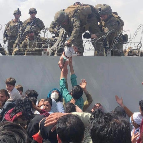 A U.S. Marine grabbing an infant over a fence of barbed wire during an evacuation at the international airport in Kabul, Afghanistan, on Aug. 19, 2021. Four days earlier, Kabul, the capital of Afghanistan, was almost the last province to fall in the hands of the Taliban.