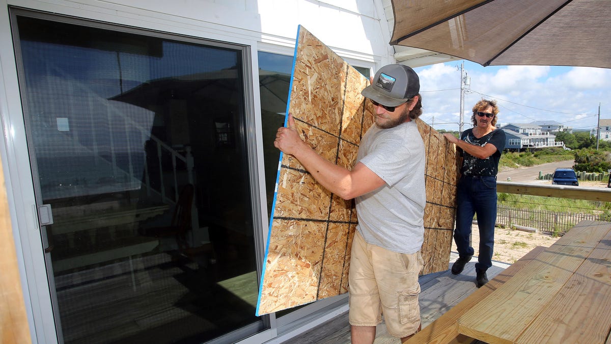James Masog, center, and Gary Tavares, right, move particle board into place to board up the sliding glass doors of a clients house in Charlestown, R.I., ahead of Hurricane Henri, Saturday, Aug. 21, 2021. New Englanders, bracing for their first direct hit by a hurricane in 30 years, are taking precautions as Tropical Storm Henri barrels toward the southern New England coast.