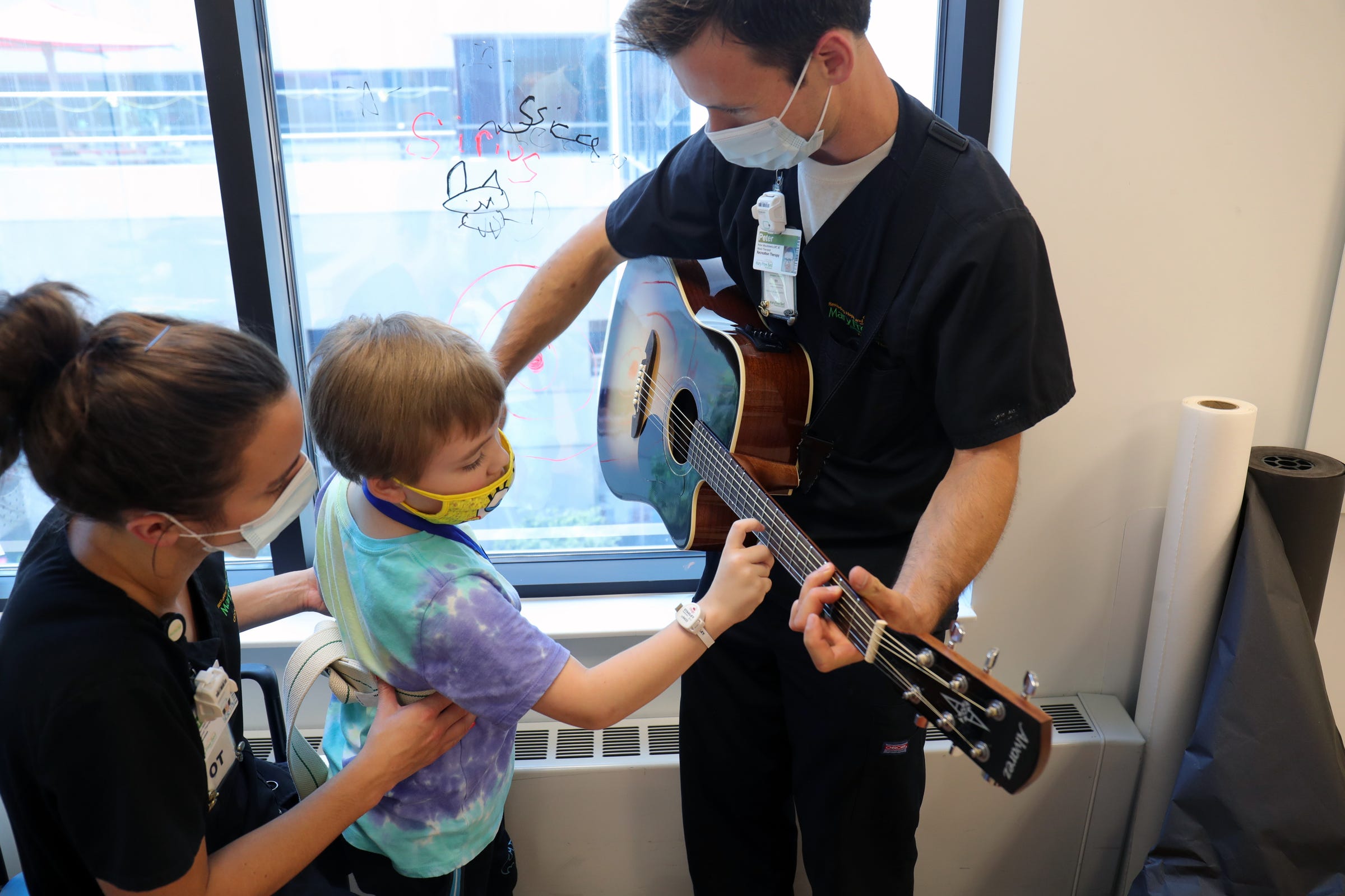 Waylon Weheir, 7, had COVID in the spring and developed life-threatening complications.  Waylon suffered multiple strokes and myocarditis. Jaime Miller-Anten from rehab services Waylon and music therapist Peter Muszkiewicz have a session that is met to improve coordination, vocal cords strength and memory. Waylon got to play on the guitar this helps him with using his hands at Mary Free Bed Rehabilitation Hospital in Grand Rapids Monday, August 2, 2021.