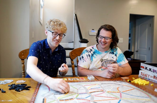 Philip Baltzer, right, and boyfriend Nick Mayes, left, play the board game "Ticket to Ride" in their South Side house. After struggling with his identity and undergoing what he only recently realized was conversion therapy with a trusted pastor, Baltzer said he is finally living the life he always thought possible.