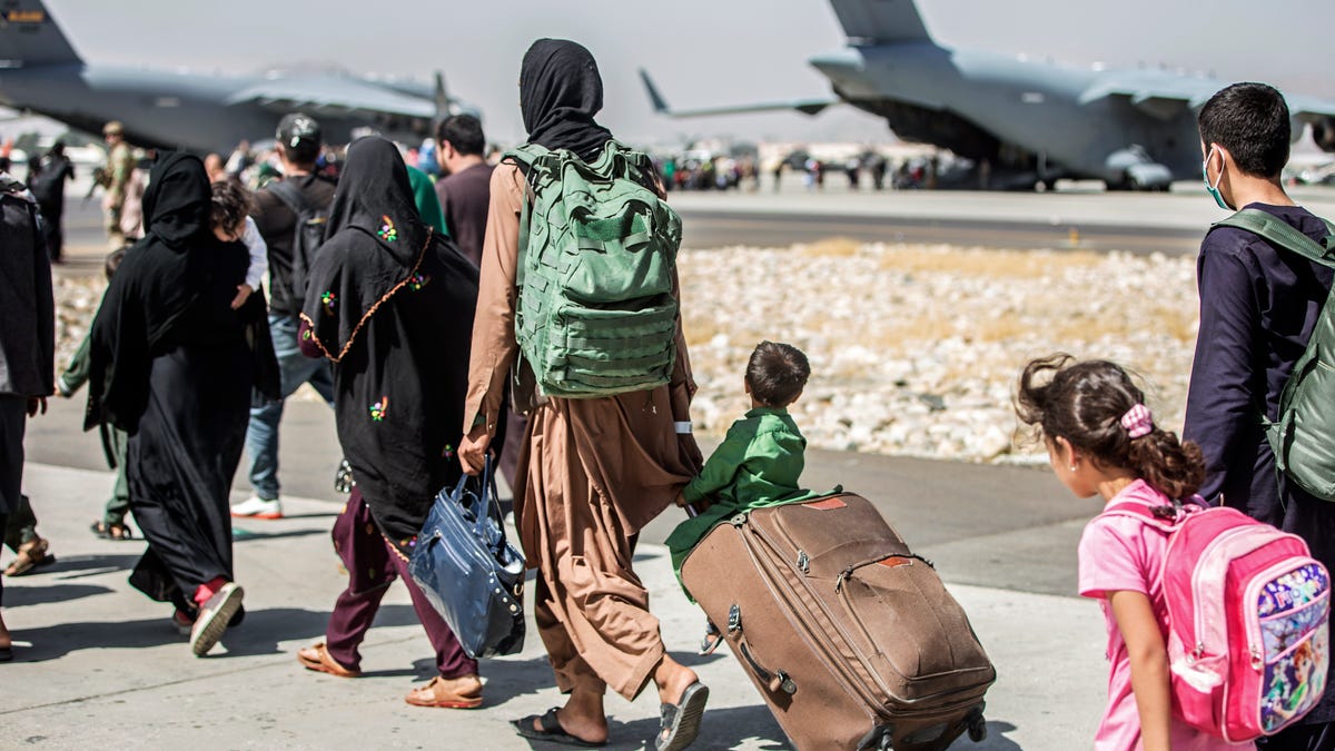 Families walk towards their flight during ongoing evacuations at Hamid Karzai International Airport, in Kabul, Afghanistan. A school district in a San Diego suburb that is home to a large refugee population says many of its families who had taken summer trips to Afghanistan to see their relatives have gotten stuck there with the chaos following the withdrawal of U.S. troops.