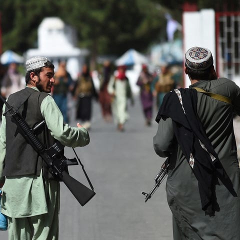 Taliban fighters walk at the main entrance gate of