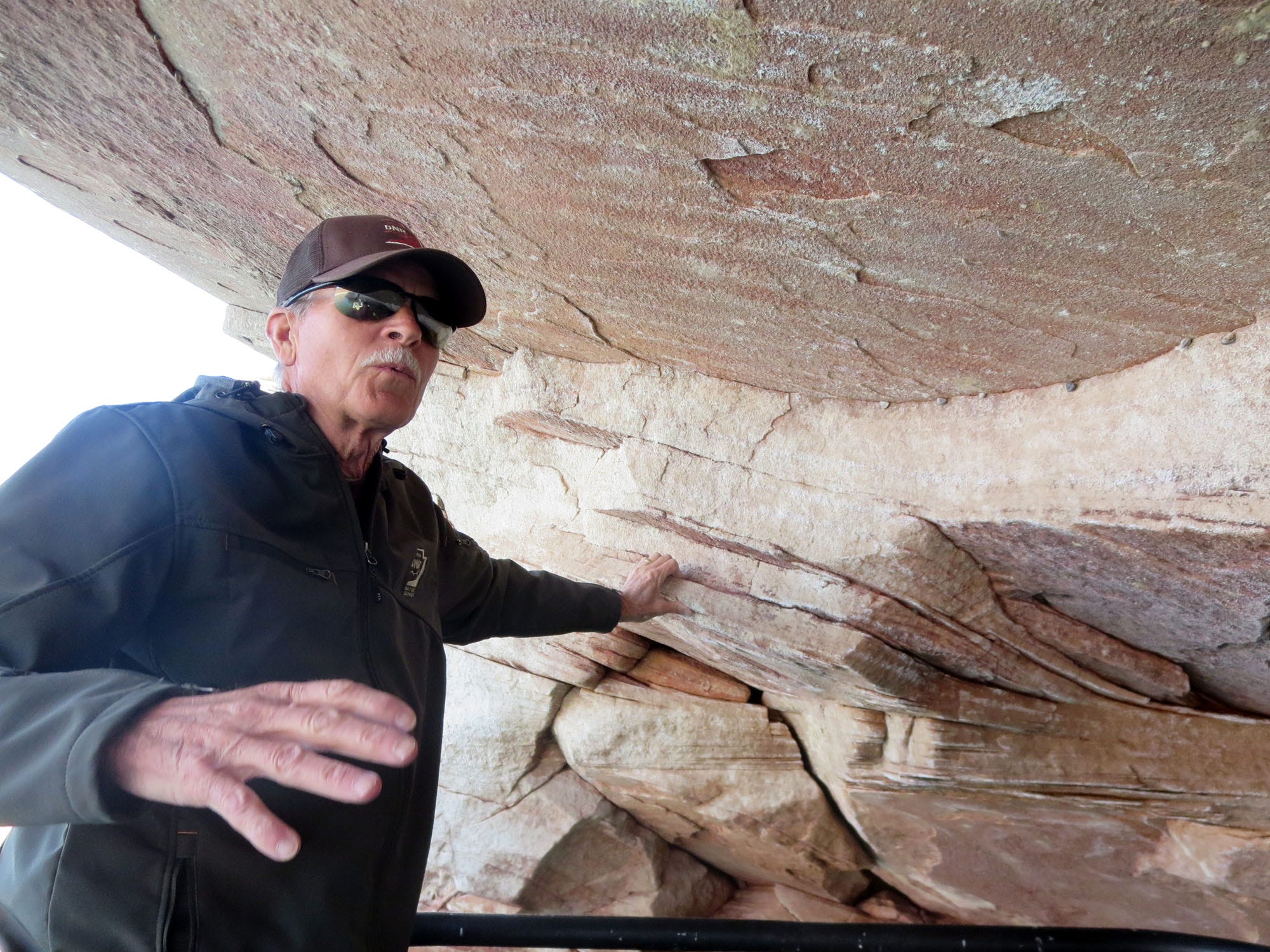 Wayne Gustaveson, a biologist with the Utah Division of Wildlife at Lake Powell, shows a visitor some of the first mussels to invade the Utah reservoir. The dead mussels are the bumps in the crease between the light and the dark rock wall above Gustaveson's hand. The area was underwater last year.