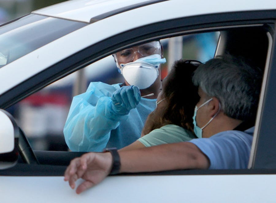 A health care worker at a 24-hour drive-thru site set up by Miami-Dade and Nomi Health in Tropical Park administers a coronavirus test Aug. 30 in Miami.