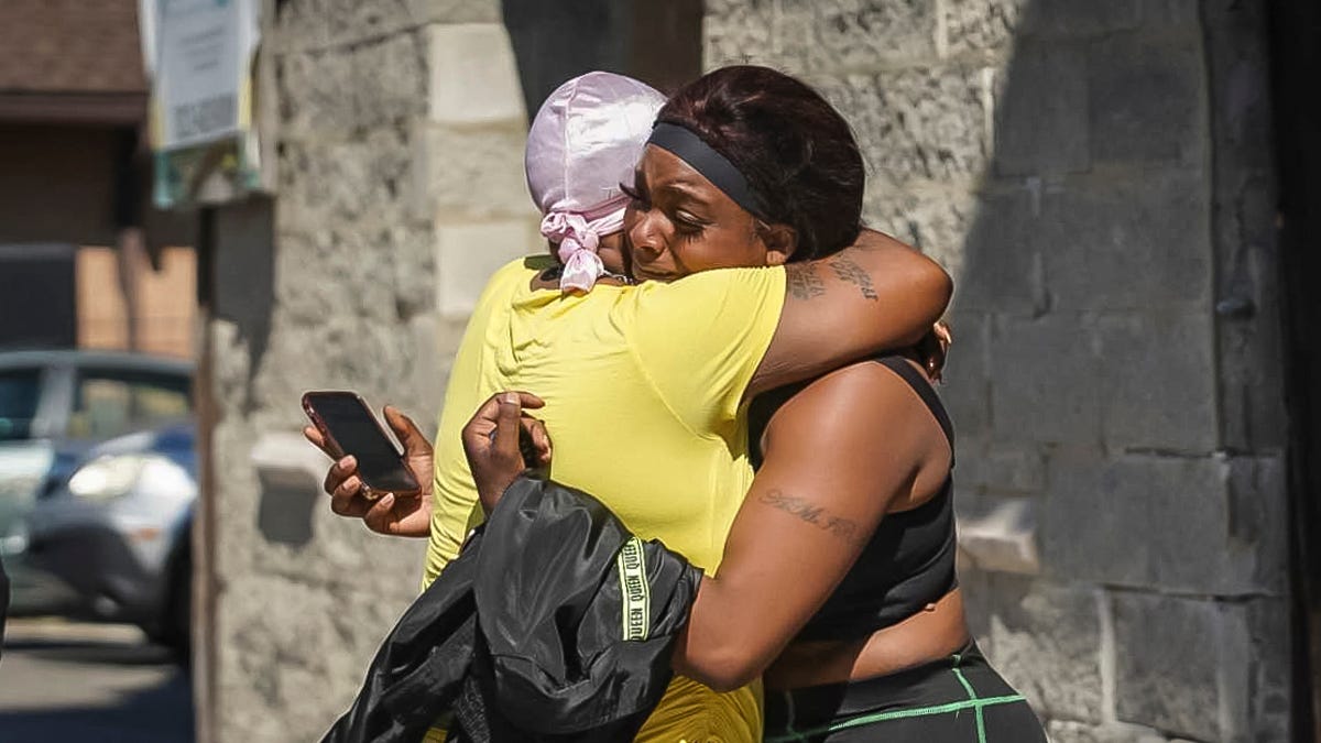 A woman  receives a hug from a supporter outside the scene of a shooting outside a home in Chicago, Tuesday, June 15, 2021.  Police say an argument at a house on Chicago's South Side erupted in fatal gunfire, leaving some dead and others injured.