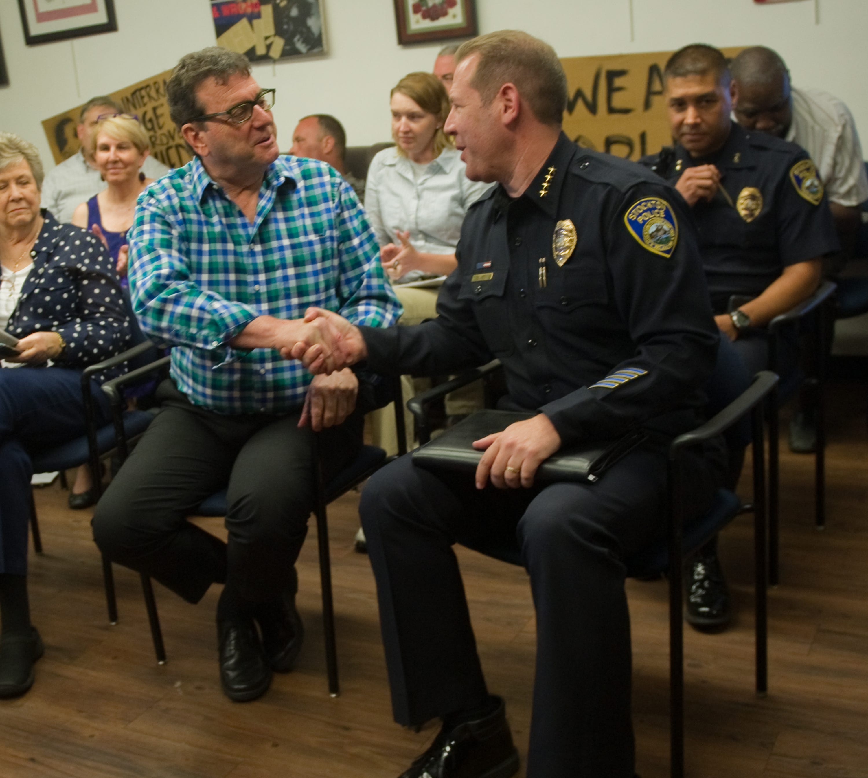 People listen as Stockton Police Chief Eric Jones, seated right, shakes hands with San Joaquin Pride Center board member Bob Kolber after a meeting at the center in downtown Stockton to address an anti-gay letter-to-the editor that Stockton police Lt. Toby Wills sent to The Record.