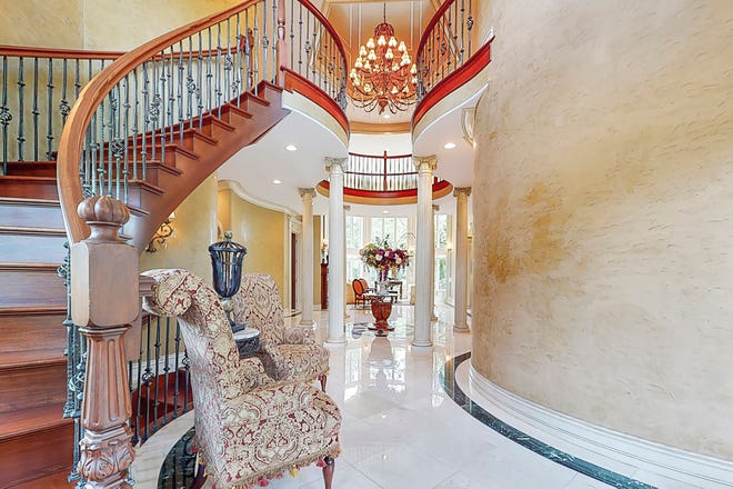 Marble, mahogany and Venetian plaster in the foyer establish the Old World mood of this lavish home. Six tall, white columns support curving balconies overhead.  A chandelier hangs through the middle.