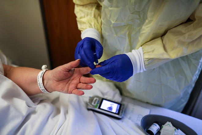 Nurses Assistant Matthew Taurianen checks the glucose levels of Debbie Sabo, 68, of Redford Twp., Mich. who is recovering from COVID-19 at Beaumont hospital in Farmington Hills, on Dec. 17, 2020.